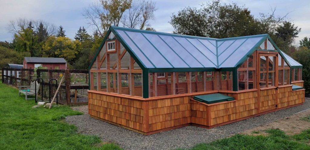 A large greenhouse with wooden shingles on the side and green accents
