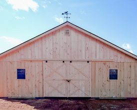 This large horse barn has lots of space with large double sliding door, windows, and metal roof with cedar vertical siding.