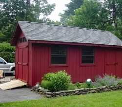 This 10x16 backyard storage shed features red painted vertical siding, gable roof, and lawn tractor ramp.