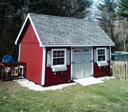 This 12x18 wood storage shed features vertical red painted siding with gray shingle roof, and accented with window shutters and transom window doors.