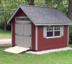 This 10x14 storage shed features vertical red painted siding, shingle roof and windows with shutters plus a transom window over the double shed door.
