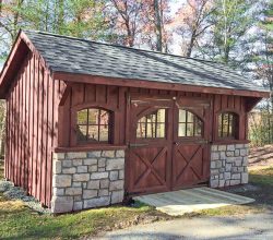 This 10x16 custom shed features board and batten siding painted red arched top windows and has rock wainscot on the front.