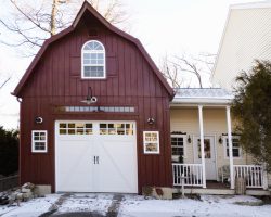 This custom built garage features barn style gambrel roof, red painted vertical siding, & lots of windows.