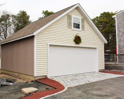 Detached garage with tan vinyl siding, storage area, & shingle roof.