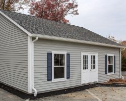 This detached garage has vinyl siding, shingled roof, large windows, & double door.