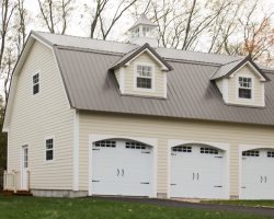 3 car garage features metal gambrel roof, carriage house garage doors, double dormers, cupola, Hardie board siding exterior.